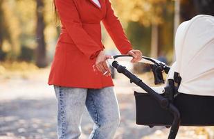 Nahaufnahme. mutter im roten mantel geht zur herbstzeit mit ihrem kind im kinderwagen im park spazieren foto