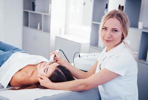 Frau, die sich im Spa-Salon hinlegt und eine Gesichtsreinigung durch eine professionelle Kosmetikerin durchführt foto