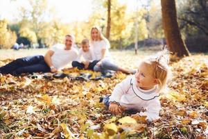 Fröhliche junge Familie, die sich auf den Boden legt und sich gemeinsam in einem Herbstpark ausruht foto