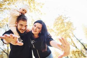 Fröhliche Familie, die sich zusammen mit ihrem Kind im schönen Herbstpark amüsiert foto