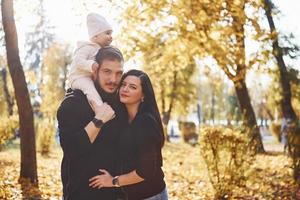 Fröhliche Familie, die sich zusammen mit ihrem Kind im schönen Herbstpark amüsiert foto