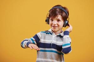 Süßer kleiner Junge mit Kopfhörern im Studio vor gelbem Hintergrund foto