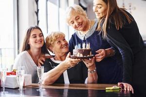 ältere frau mit familie und freunden, die drinnen einen geburtstag feiern foto