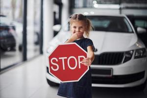 Porträt eines süßen kleinen Mädchens, das im Autosalon ein Straßenschild in den Händen hält foto