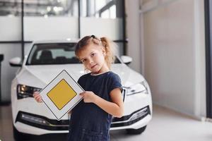 Porträt eines süßen kleinen Mädchens, das im Autosalon ein Straßenschild in den Händen hält foto