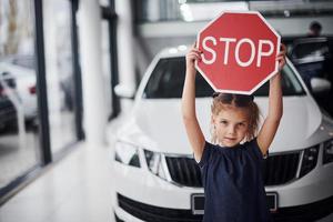 Porträt eines süßen kleinen Mädchens, das im Autosalon ein Straßenschild in den Händen hält foto