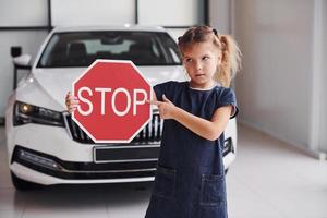 Porträt eines süßen kleinen Mädchens, das im Autosalon ein Straßenschild in den Händen hält foto