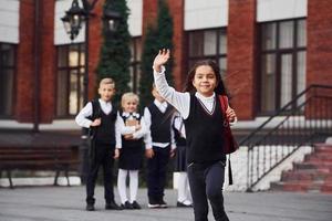 gruppe von kindern in schuluniform, die zusammen vor der kamera im freien in der nähe des bildungsgebäudes posieren foto