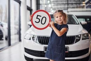 Porträt eines süßen kleinen Mädchens, das im Autosalon ein Straßenschild in den Händen hält foto