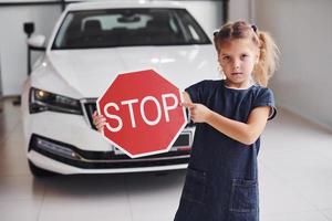 Porträt eines süßen kleinen Mädchens, das im Autosalon ein Straßenschild in den Händen hält foto