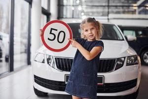 Porträt eines süßen kleinen Mädchens, das im Autosalon ein Straßenschild in den Händen hält foto