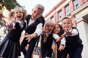 Spaß haben und sich umarmen. Gruppe von Kindern in Schuluniform, die sich im Freien in der Nähe des Bildungsgebäudes befinden foto