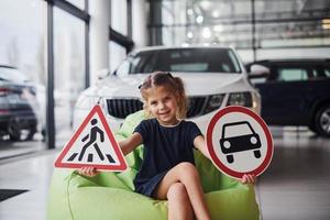 Porträt eines süßen kleinen Mädchens, das Verkehrsschilder im Automobilsalon in den Händen hält foto