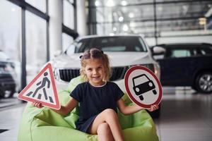 Porträt eines süßen kleinen Mädchens, das Verkehrsschilder im Automobilsalon in den Händen hält foto