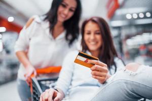 zwei junge frauen haben spaß beim rennen und reiten im einkaufskorb im supermarkt foto