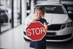 Porträt eines süßen kleinen Mädchens, das im Autosalon ein Straßenschild in den Händen hält foto