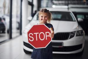 Porträt eines süßen kleinen Mädchens, das im Autosalon ein Straßenschild in den Händen hält foto