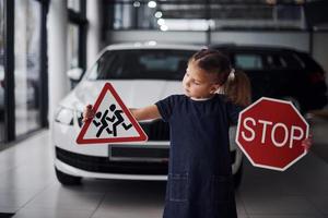 Porträt eines süßen kleinen Mädchens, das Verkehrsschilder im Automobilsalon in den Händen hält foto