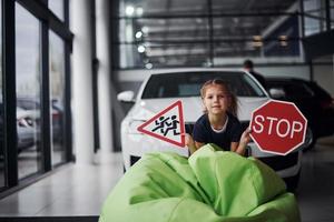 Porträt eines süßen kleinen Mädchens, das Verkehrsschilder im Automobilsalon in den Händen hält foto