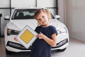Porträt eines süßen kleinen Mädchens, das im Autosalon ein Straßenschild in den Händen hält foto