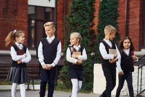 Gruppe von Kindern in Schuluniform, die sich im Freien in der Nähe des Bildungsgebäudes befinden foto