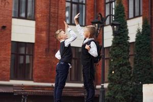 zwei kleine jungen in schuluniform, die draußen zusammen sind, geben high five in der nähe des bildungsgebäudes foto