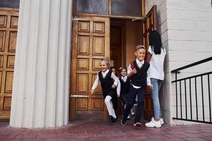 Gruppe von Kindern in Schuluniform, die aus einem Gebäude durch die Tür rennen foto