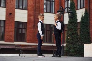 Zwei kleine Jungen in Schuluniform, die sich im Freien in der Nähe des Bildungsgebäudes befinden foto