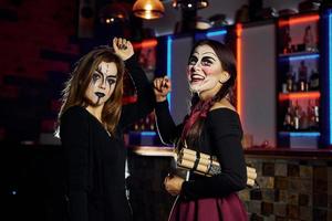 Zwei Freundinnen sind auf der thematischen Halloween-Party in gruseligem Make-up und Kostümen mit Zeitbombe foto
