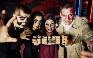 Freunde mit Bombe in den Händen sind auf der thematischen Halloween-Party in gruseligem Make-up und Kostümen foto