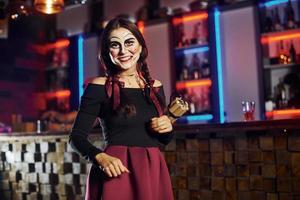 Porträt einer Frau, die auf der thematischen Halloween-Party in gruseligem Make-up und Kostüm mit Bombe in den Händen ist foto