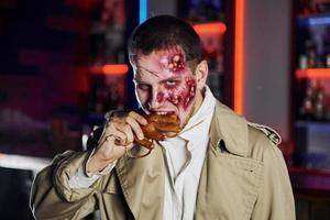 tote Hand essen. Porträt des Mannes, der auf der thematischen Halloween-Party in Zombie-Make-up und Kostüm ist foto