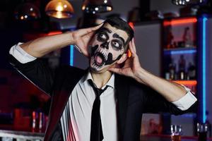 Porträt eines Mannes, der auf der thematischen Halloween-Party in gruseligem Skelett-Make-up und Kostüm ist foto