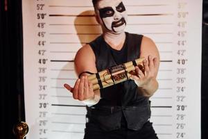 Porträt eines Mannes, der auf der thematischen Halloween-Party in gruseligem Black-Metal-Make-up und Kostüm mit Bombe in den Händen ist foto