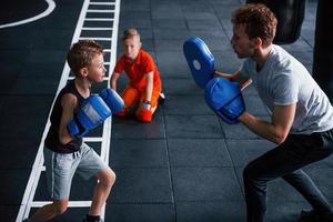 Der junge Trainer unterrichtet Kinder im Boxsport im Fitnessstudio foto