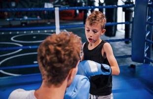 Der junge Boxtrainer hilft dem kleinen Jungen in Schutzkleidung zwischen den Runden am Ring foto