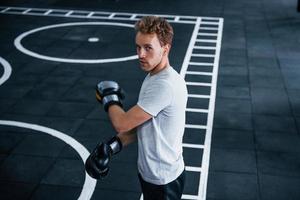 junger mann in weißem hemd und boxschutzhandschuhen, die übungen im fitnessstudio machen foto