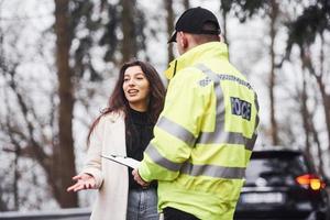 männlicher polizist in grüner uniform, der mit der besitzerin des autos auf der straße spricht foto