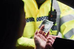 männlicher polizist in grüner uniform, der fahrzeug auf der straße überprüft. Frau, die versucht, Bestechungsgelder zu geben foto