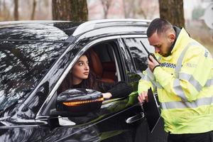 männlicher polizist in grüner uniform, der per funksender in der nähe des autos mit fahrerin spricht foto