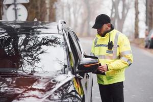 männlicher polizist in grüner uniform, der fahrzeug auf der straße überprüft foto