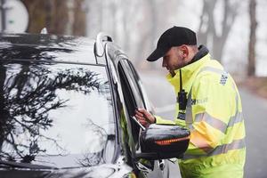 männlicher polizist in grüner uniform, der fahrzeug auf der straße überprüft foto