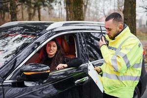 männlicher polizist in grüner uniform, der per funksender in der nähe des autos mit fahrerin spricht foto