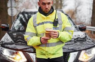 männlicher polizist in grüner uniform, der eine pause mit donut auf der straße macht foto