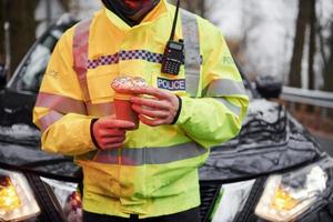 männlicher polizist in grüner uniform, der eine pause mit donut auf der straße macht foto