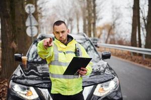 männlicher Polizist in grüner Uniform mit Notizblock, der nach vorne zeigt foto