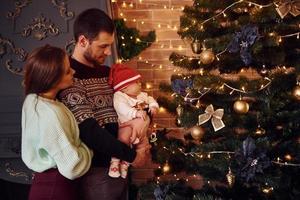 vater und mutter mit ihrem kind zusammen im weihnachtlich dekorierten zimmer foto