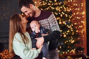 vater und mutter mit ihrem kind zusammen im weihnachtlich dekorierten zimmer foto