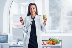 Ernährungsberaterin im weißen Mantel, die drinnen im Büro am Arbeitsplatz sitzt foto