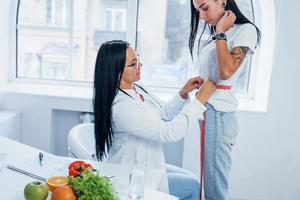 Ernährungsberaterin, die die Taille des Patienten mit Klebeband im Büro misst foto